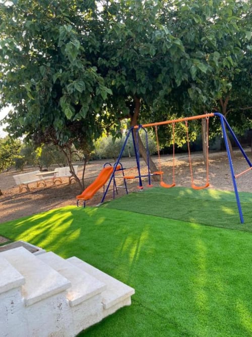 Backyard garden at Rentalaya villa in Reus with artificial grass, orange and blue playground equipment, and mature trees