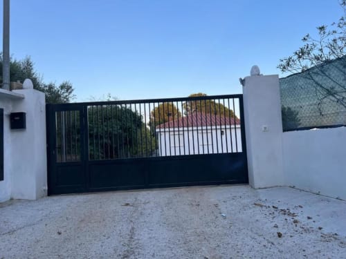 Black and white modern gate entrance to Rentalaya villa in Reus with white pillars and garden views