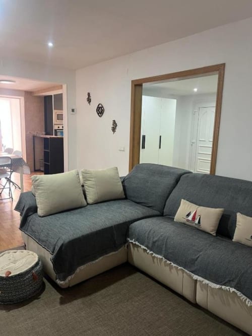 Modern living area in Reus villa with L-shaped gray sofa, cream pillows, and mirrored wardrobe doors overlooking garden views