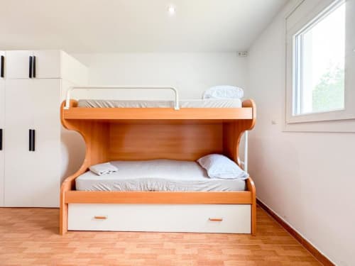 Bright bedroom in Rentalaya villa in Reus with wooden bunk bed, white linens, storage drawer, and garden view window