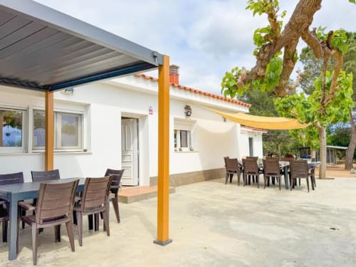 Sunny terrace of Rentalaya villa in Reus with wooden pergola, dining tables, and mature tree in garden view setting