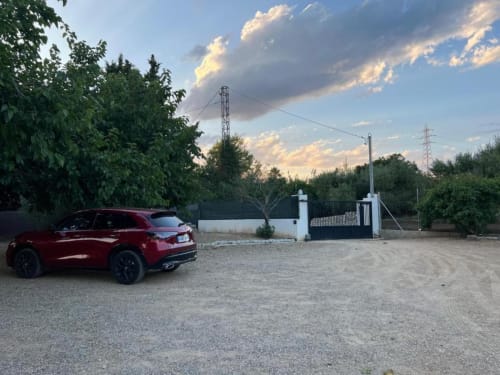 Red SUV parked at Rentalaya villa in Reus with gated entrance and garden views at sunset