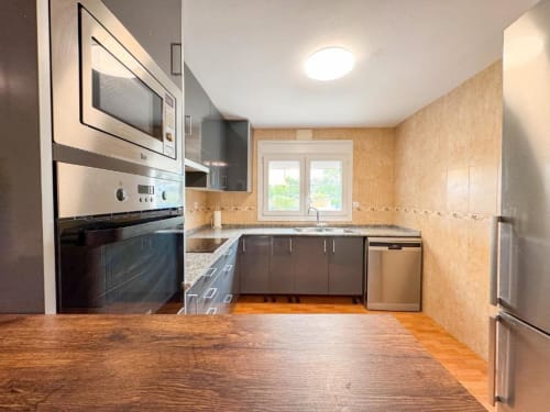 Modern kitchen in Reus villa with stainless steel appliances, granite countertop, brown cabinets, and window views of the