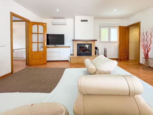 Spacious villa living area in Reus with fireplace, flat-screen TV, cream sofa, wooden doors, and garden views