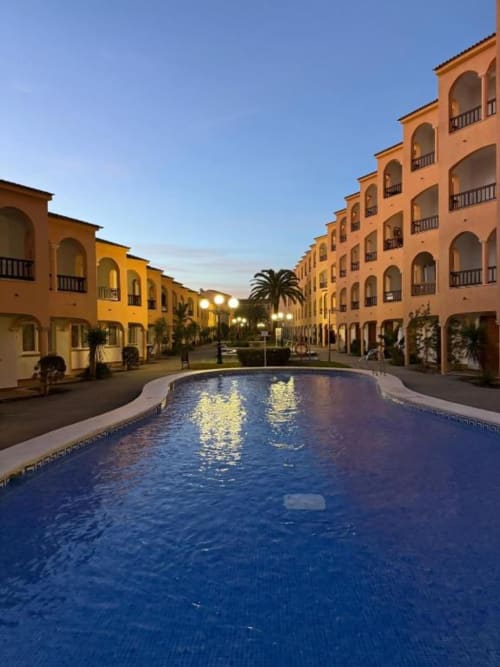 Peñíscola resort courtyard with illuminated pool, terracotta buildings, and palm trees at dusk