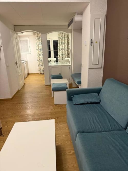 Spacious living room in Peñíscola apartment with blue sofa, white table, wooden floors, and mirrored entryway