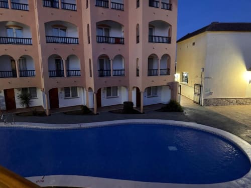 Peñíscola apartment complex at dusk with illuminated pool, pink and white buildings, terraces, and archways