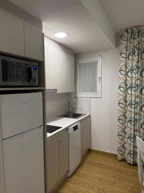 Compact kitchen area in Peñíscola apartment with white refrigerator, microwave, stovetop, and sink with window view