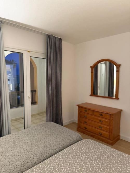 Modern bedroom in Peñíscola apartment with twin beds, wooden dresser, mirror, and en-suite bathroom access