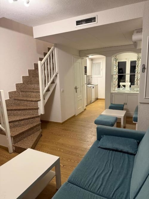 Modern 2-bedroom apartment living area in Peñíscola with stairs, kitchen, blue beds, and wooden flooring