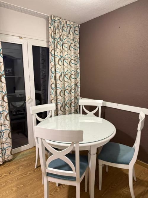 White round dining table with blue chairs in Peñíscola apartment, brown accent wall, patio doors with geometric curtains