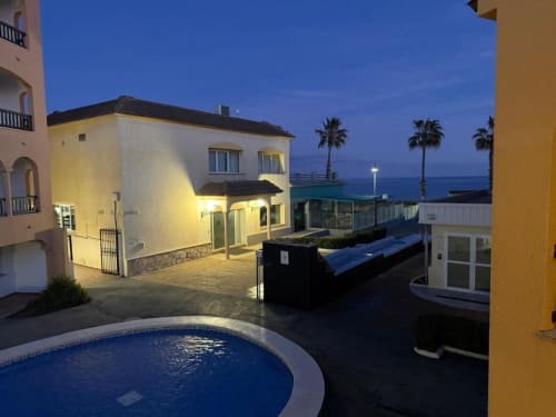 Evening view of Rentalaya 2-bedroom apartment in Peñíscola with pool, terrace, and Mediterranean Sea overlooking palm trees