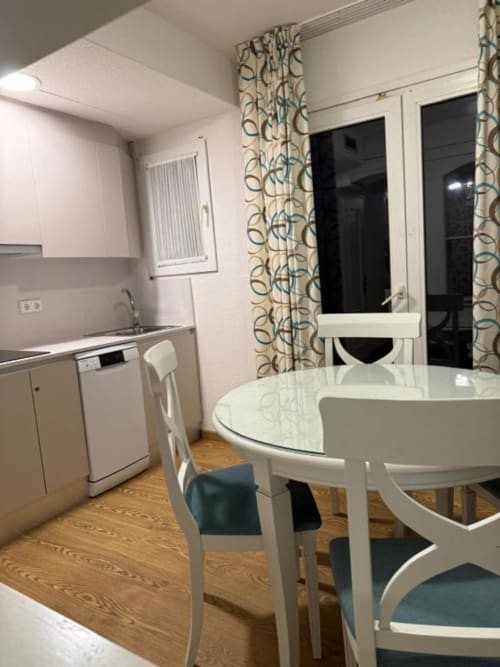 Modern kitchen-dining area in Peñíscola apartment with white round table, dishwasher, and patterned curtains overlooking