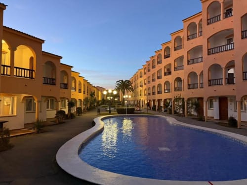 Rentalaya apartment complex in Peñíscola at dusk with illuminated terracotta buildings surrounding a curved swimming pool