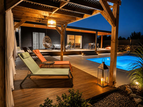 Terrasse de villa de luxe la nuit avec piscine chauffée, pergola en bois, chaises longues et vue illuminée sur la campagne corse