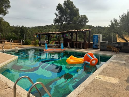 Piscina con mosaico de suelo colorido y flotadores en el hotel rural Masias Can Trabal de Olerdola, España