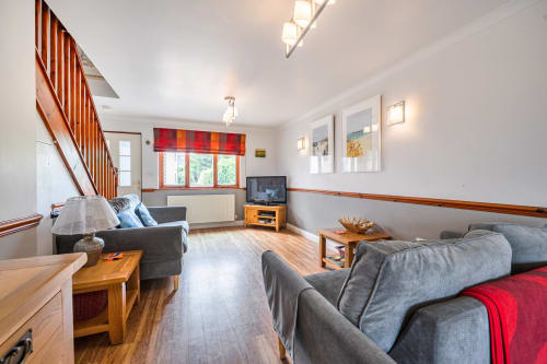 Bright open-plan living room at Sunflower Cottage in Exeter with wood flooring, gray sofas, wooden staircase, TV, and garden