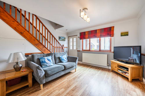 Bright living room at Sunflower Cottage in Exeter with gray sofa, wooden stairs, TV, fireplace, and garden views through