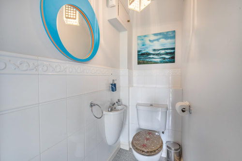 Bright bathroom in Sunflower Cottage with white tile walls, blue circular mirror, toilet with patterned seat, and seascape
