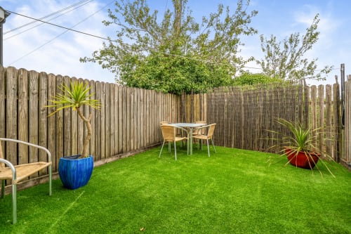 Private fenced garden at Sunflower Cottage in Exeter with lush green lawn, wooden seating, potted plants, and outdoor dining