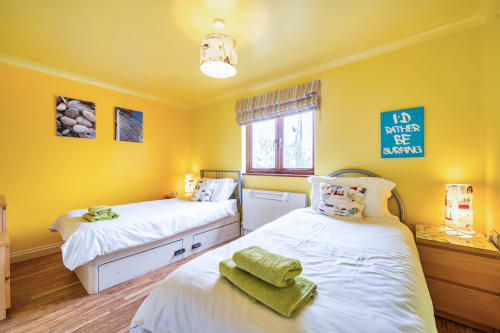 Bright yellow twin bedroom at 2 Doves Holiday Property in Exeter with white beds, garden view and "I'd rather be surfing"
