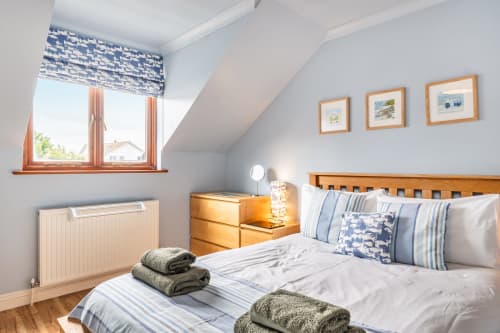 Bright attic bedroom at Sunflower Cottage in Exeter with wooden bed, blue striped bedding, framed coastal art, and garden