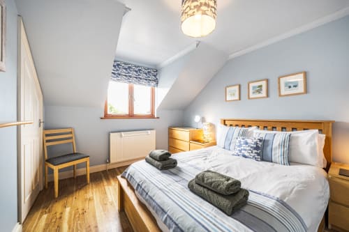 Bright attic bedroom at 2 Doves Holiday Property with wooden bed, blue striped bedding, wooden chair, and garden views