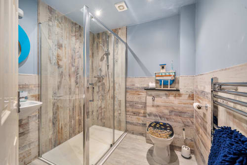 Modern bathroom in Sunflower Cottage, Exeter, featuring wooden-effect tiles, walk-in shower, heated towel rail, and blue