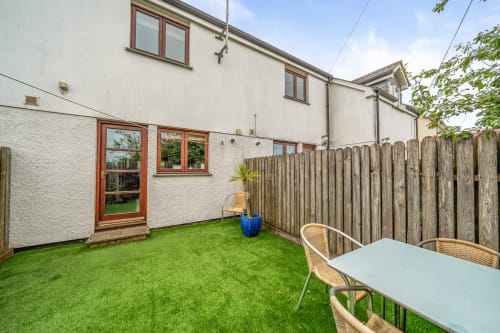 Private fenced garden at Sunflower Cottage in Exeter with artificial grass, wooden seating, and white outdoor furniture