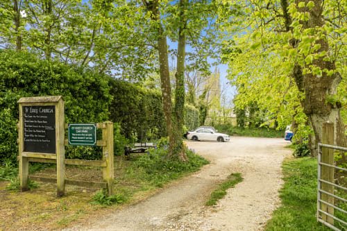 St Issey Church driveway with gravel path, trees, and parked car near Exeter holiday cottage
