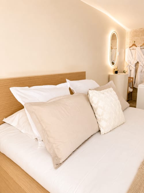 Chambre moderne à l'hôtel L'Escapade au Mans avec lit en bois, literie neutre et éclairage ambiant chaleureux