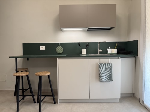 Angolo cottura moderno con backsplash verde scuro, armadi bianchi, tavolo bar per due persone e elettrodomestici in acciaio inox