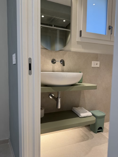 Bagno moderno con lavabo bianco, ripiano verde, specchio rotondo e finestra a La Casetta dei Ronchi, Marina di Massa