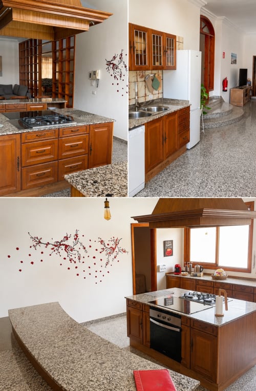 Cocina Villa la Higuera con gabinetes de madera, encimeras de granito, estufa a gas y arte decorativo rojo en la pared
