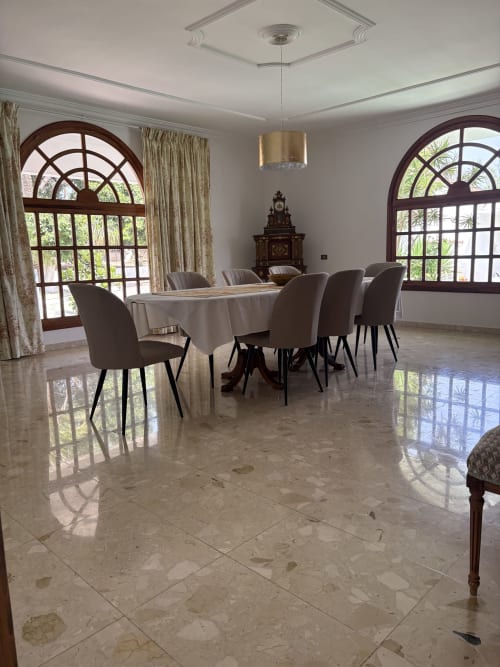 Elegante comedor en Villa la Higuera con suelo de mármol, mesa redonda y ventanas arqueadas con vistas a los jardines
