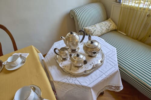 Elegant tea service setup at A Casa Armenia B&B in Turin with silver teapot, cups, and striped armchair