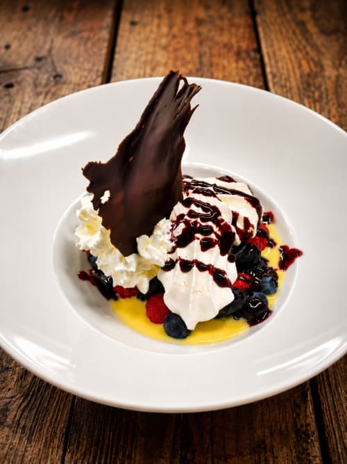Élégant plateau de desserts à La Source Bleue avec crème fouettée, baies, éclats de chocolat et sauce jaune sur fond blanc