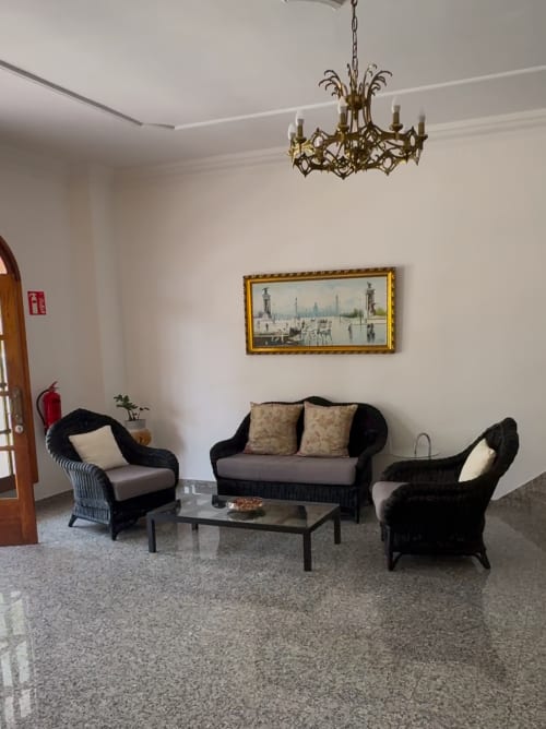 Elegante área de estar en el vestíbulo de Villa la Higuera con muebles de mimbre negro, lámpara de araña dorada y cuadros enmarcados