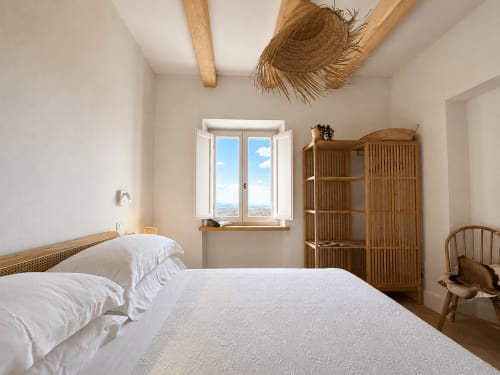 Bright bedroom with white bedding, wooden beams, and open windows overlooking Tuscan countryside at Montemassi townhouse