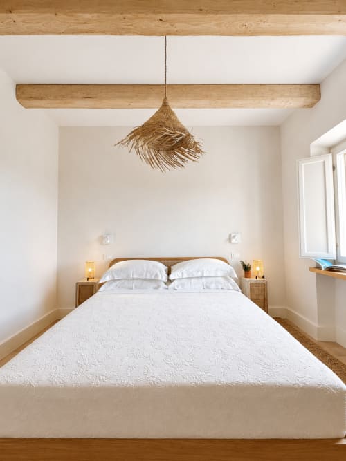 Bright, minimalist bedroom at Tuscan Townhouse with wooden beam ceiling, woven pendant light, and garden views