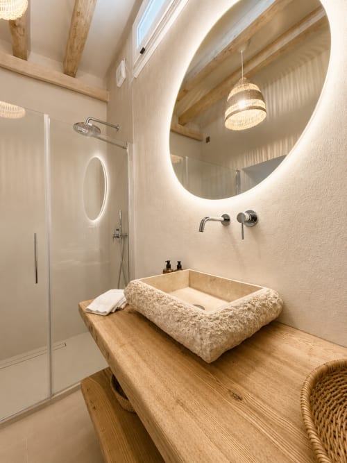 Modern bathroom at Tuscan Townhouse with stone sink, illuminated oval mirror, wooden vanity, and walk-in shower with natural