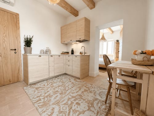 Tuscan townhouse kitchen with light wood cabinetry, dining table, and garden view through doorway in Montemassi