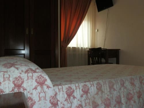 Habitación individual en Hostal San Poul de Consuegra con camas gemelas, ropa de cama roja con patrón, escritorio y vistas a la ciudad desde la ventana