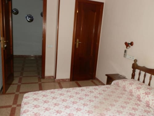 Habitación individual del Hostal San Poul en Consuegra con cama, puertas de madera, piso de azulejos y vistas a la ciudad