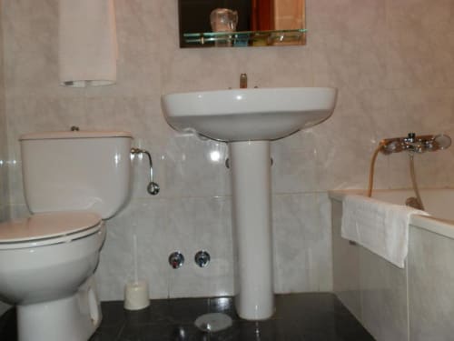 Baño limpio del Hostal San Poul en Consuegra con lavabo de pedestal, inodoro, toallero y paredes alicatadas