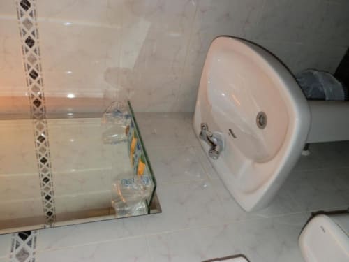 Baño moderno con lavamanos blanco, espejo y piso de cerámica beige en Hostal San Poul, Consuegra