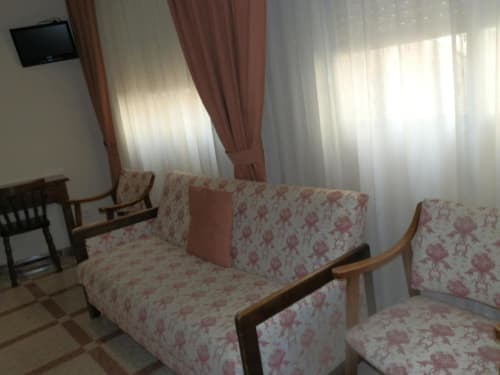 Habitación triple en Hostal San Poul con sofá floral, sillón y cortinas translúcidas que dejan pasar la luz natural