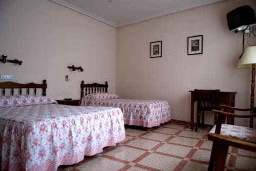 Habitación triple del Hostal San Poul en Consuegra con tres camas, ropa de cama floral rosa, muebles de madera y piso de baldosas