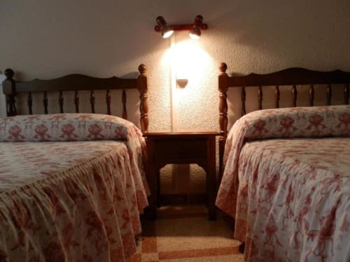Camas gemelas con colchas rojas estampadas en el Hostal San Poul de Consuegra, España, con lámpara de lectura en la pared