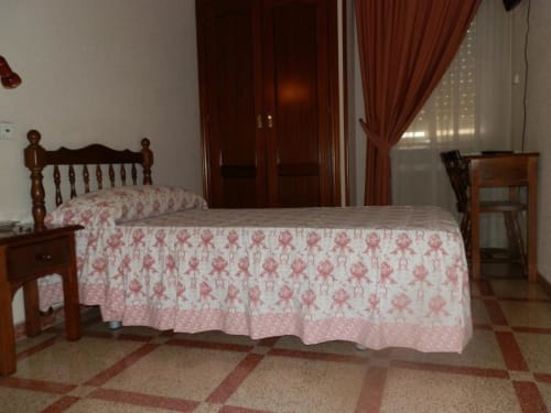 Habitación individual en Hostal San Poul con cama de madera, ropa de cama floral rosa y piso de azulejos en Consuegra